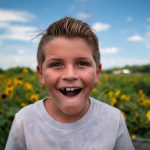 Boy in white crew neck shirt standing on yellow flower field during daytime