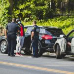 man in black t-shirt and black pants standing beside black suv during daytime